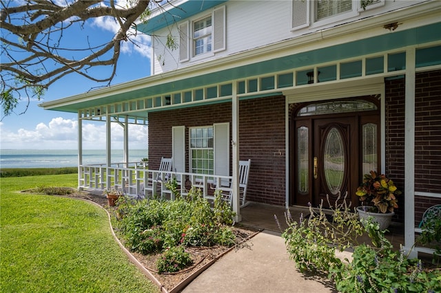 doorway to property with a lawn, a water view, and a porch