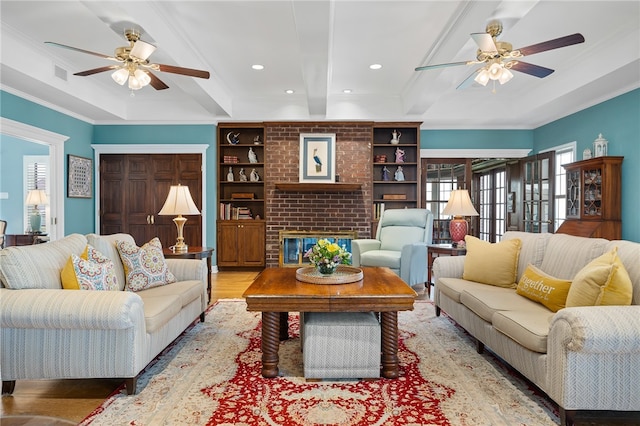 living room with hardwood / wood-style flooring, ceiling fan, crown molding, beam ceiling, and a fireplace