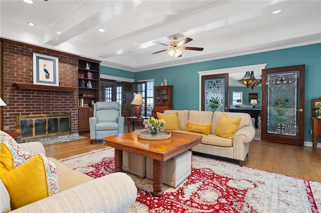 living room with a fireplace, light wood-type flooring, crown molding, and beamed ceiling