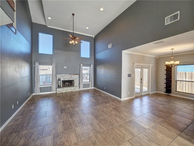 unfurnished living room with a high ceiling, french doors, ceiling fan with notable chandelier, a stone fireplace, and ornamental molding