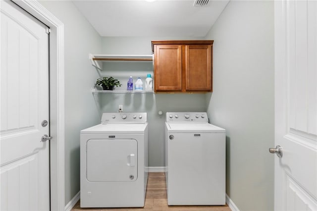 clothes washing area featuring cabinet space, independent washer and dryer, light wood finished floors, and baseboards