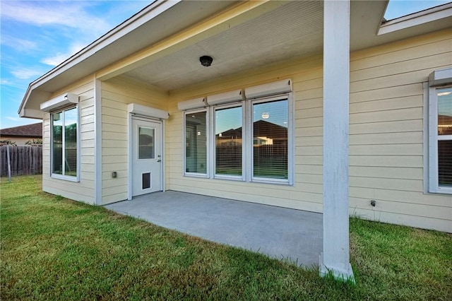 entrance to property featuring a patio area, a lawn, and fence