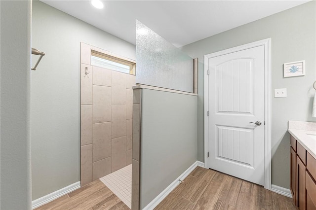 full bathroom featuring vanity, wood finished floors, a walk in shower, and baseboards