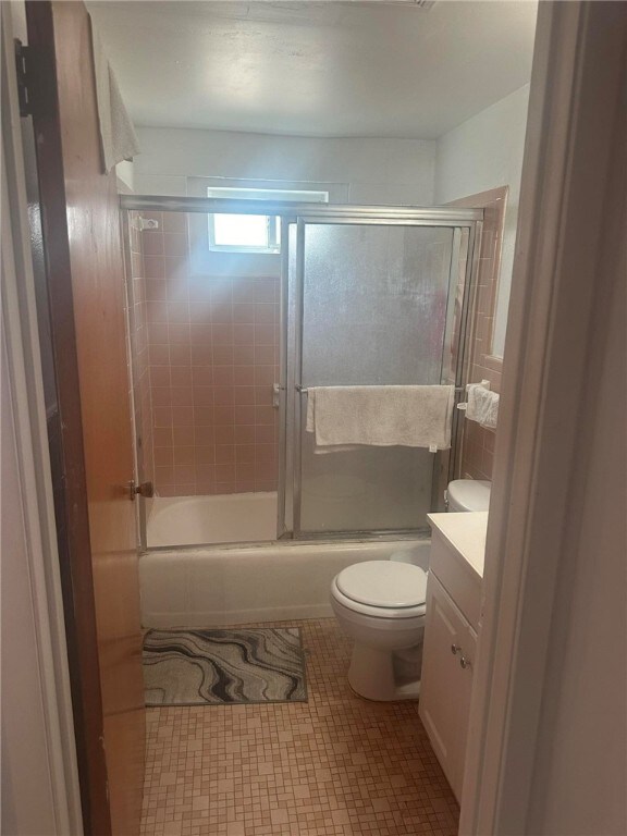 full bathroom with shower / bath combination with glass door, tile patterned floors, toilet, and vanity