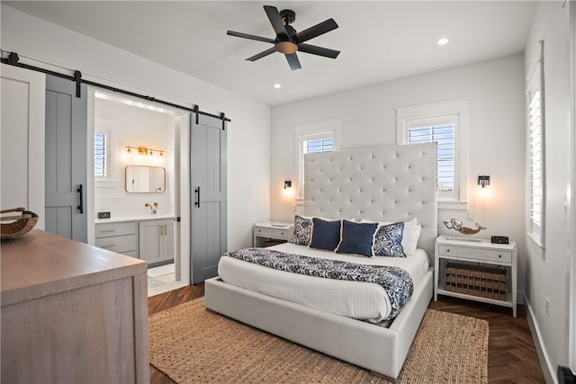 bedroom featuring connected bathroom, dark parquet flooring, a barn door, and ceiling fan