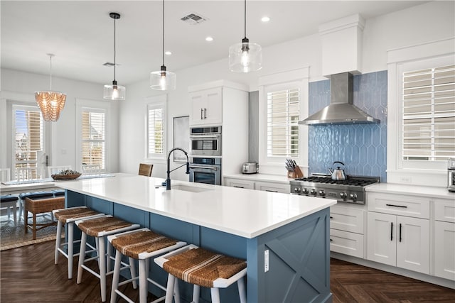 kitchen featuring appliances with stainless steel finishes, tasteful backsplash, an island with sink, dark parquet floors, and wall chimney range hood