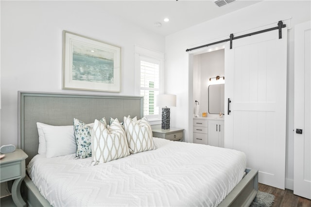 bedroom with a barn door, connected bathroom, and dark hardwood / wood-style flooring