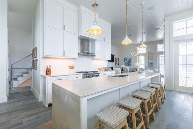 kitchen featuring a sink, wall chimney range hood, wood finished floors, visible vents, and white cabinetry