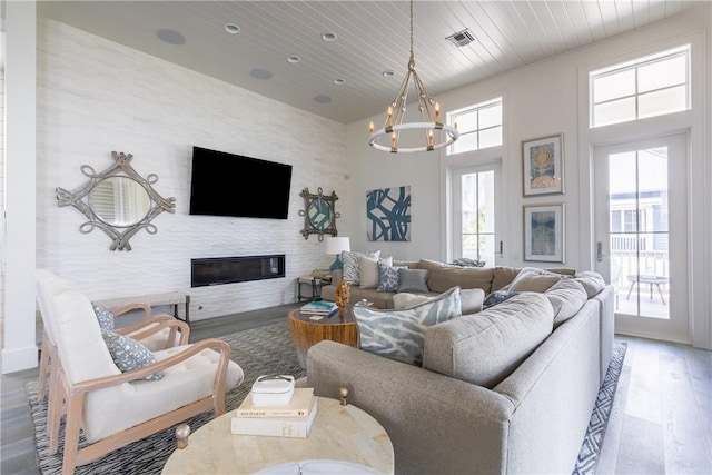 living room featuring a glass covered fireplace, visible vents, wood ceiling, a chandelier, and wood finished floors