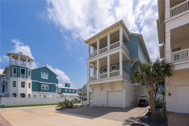 coastal inspired home featuring fence, a residential view, a balcony, a garage, and decorative driveway