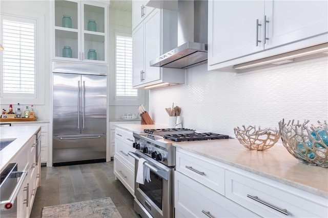 kitchen featuring high end appliances, wall chimney exhaust hood, and white cabinets
