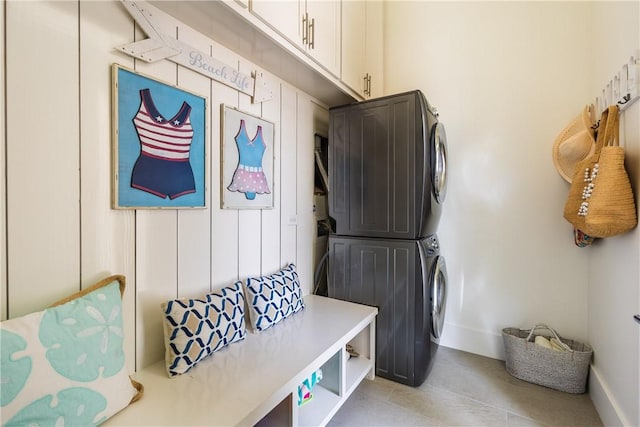 laundry area with stacked washing maching and dryer, light tile patterned flooring, cabinet space, and baseboards