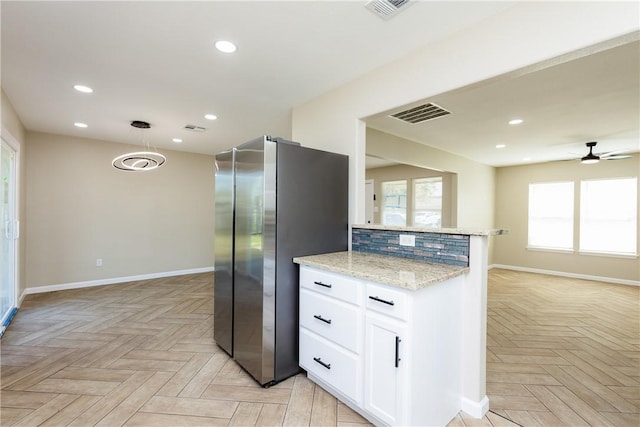 kitchen featuring open floor plan, light stone counters, recessed lighting, freestanding refrigerator, and white cabinets