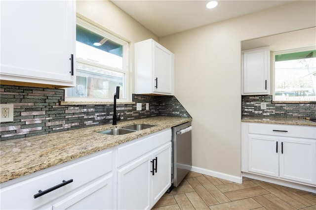 kitchen with plenty of natural light, dishwasher, light stone countertops, and a sink