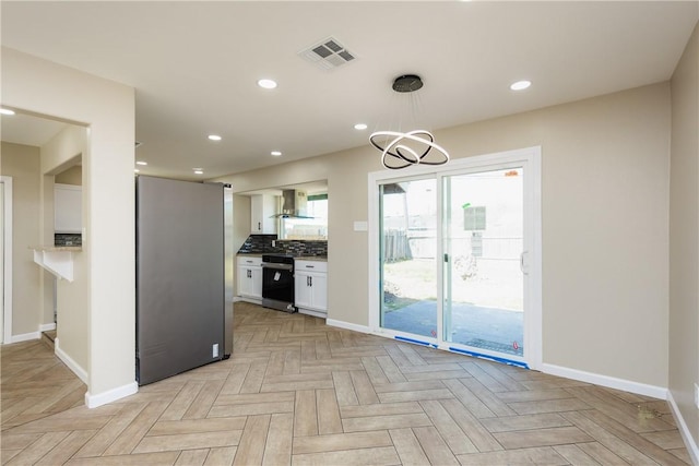 kitchen with visible vents, wall chimney range hood, decorative backsplash, freestanding refrigerator, and white cabinets