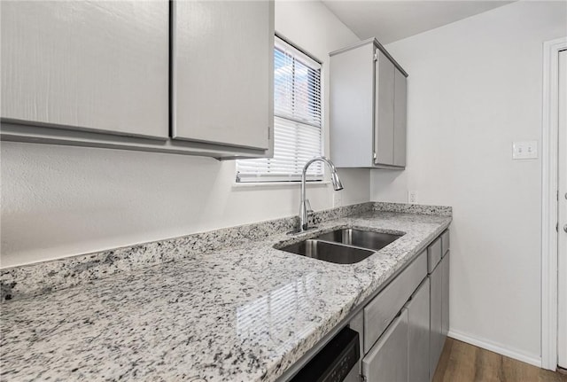 kitchen featuring sink, light stone counters, stainless steel dishwasher, dark hardwood / wood-style floors, and gray cabinets