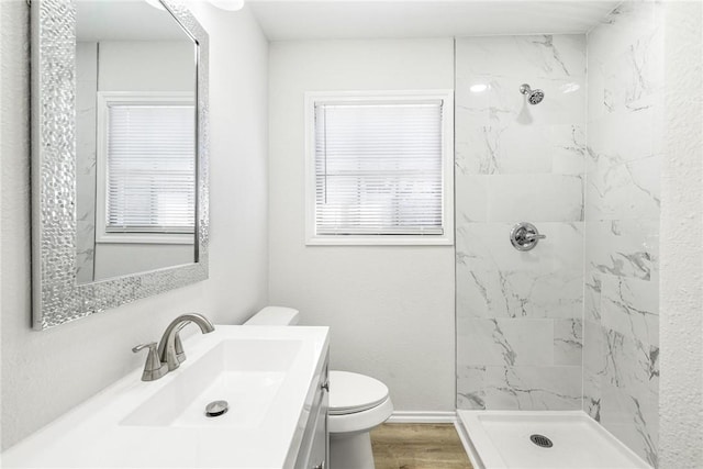 bathroom featuring hardwood / wood-style flooring, tiled shower, vanity, a healthy amount of sunlight, and toilet