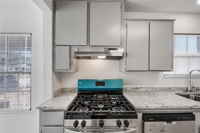 kitchen with stainless steel appliances, light stone countertops, and sink