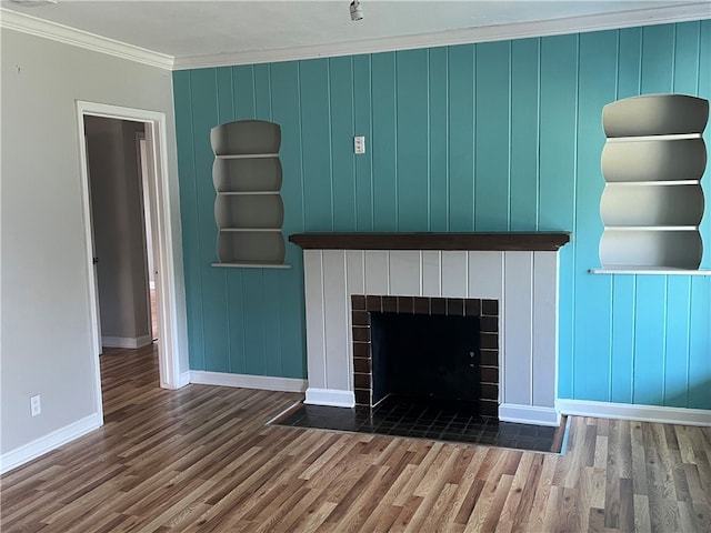 unfurnished living room with wood walls, wood-type flooring, a tile fireplace, and ornamental molding