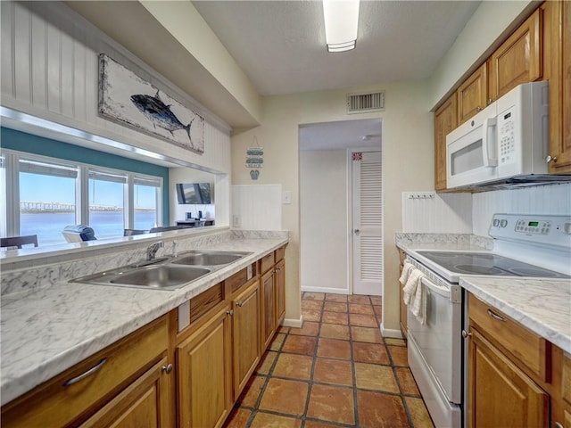 kitchen featuring brown cabinets, light countertops, visible vents, a sink, and white appliances