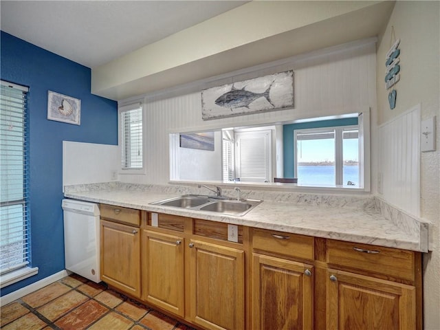 kitchen featuring light countertops, brown cabinetry, white dishwasher, a sink, and baseboards