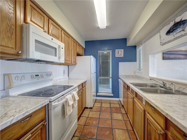 kitchen with light countertops, white appliances, brown cabinetry, and a sink