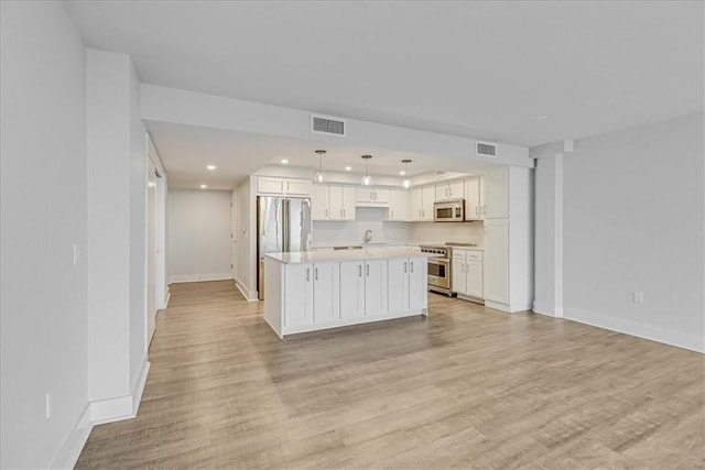 kitchen featuring white cabinetry, a center island, stainless steel appliances, decorative light fixtures, and light wood-type flooring