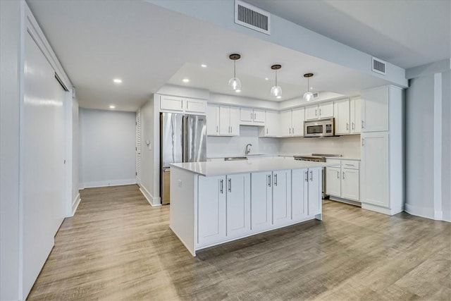 kitchen with pendant lighting, a center island, white cabinets, light hardwood / wood-style flooring, and stainless steel appliances