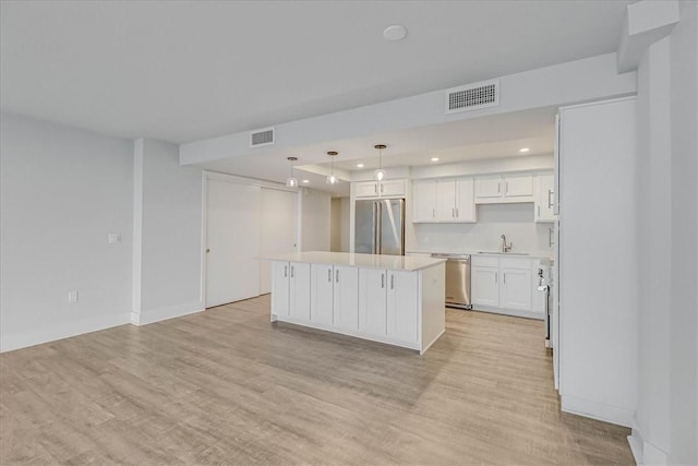 kitchen featuring light wood-type flooring, stainless steel appliances, a center island, white cabinetry, and hanging light fixtures