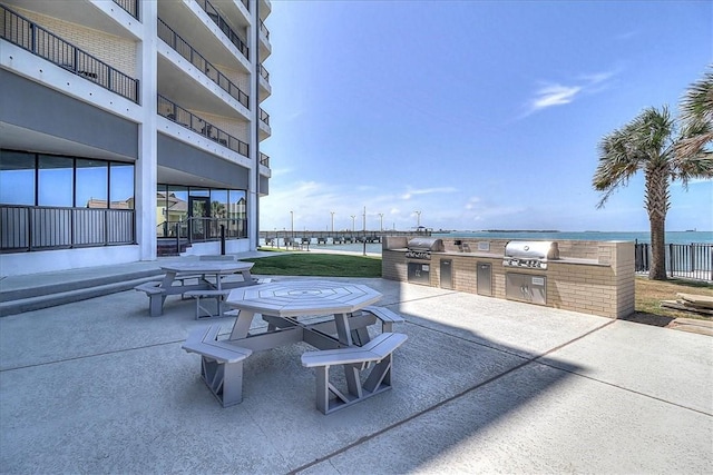 view of patio with grilling area, a water view, and exterior kitchen