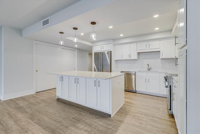 kitchen featuring stainless steel appliances, decorative light fixtures, light hardwood / wood-style flooring, white cabinets, and a kitchen island