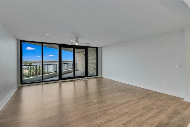 spare room with light wood-type flooring, expansive windows, and ceiling fan