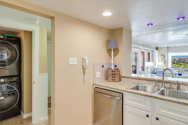 kitchen featuring dishwasher, sink, white cabinets, stacked washer and dryer, and light stone counters