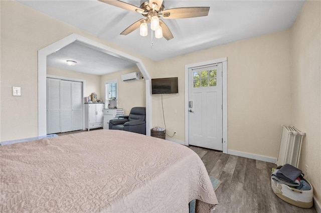 bedroom featuring a wall mounted AC, wood finished floors, baseboards, and a ceiling fan