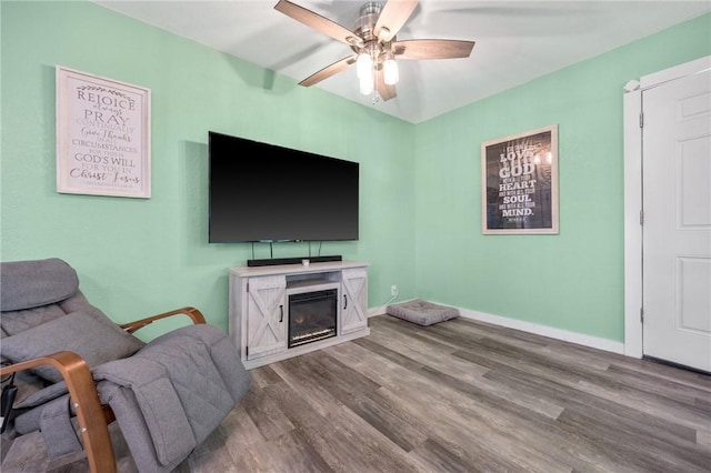 living room featuring wood finished floors, a ceiling fan, a glass covered fireplace, and baseboards