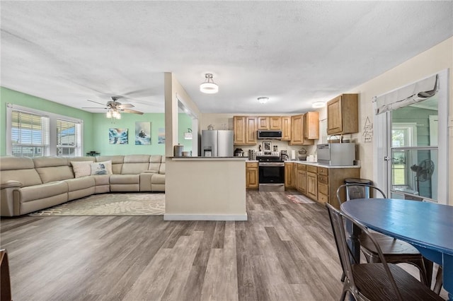 kitchen featuring appliances with stainless steel finishes, wood finished floors, a ceiling fan, plenty of natural light, and a textured ceiling