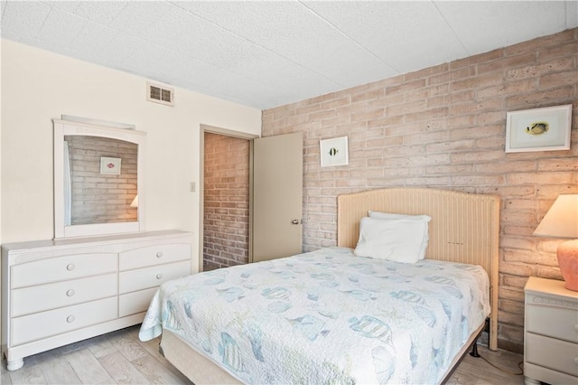 bedroom featuring brick wall and light wood-type flooring