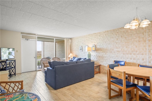 living room featuring a wall of windows, brick wall, light hardwood / wood-style flooring, and a notable chandelier