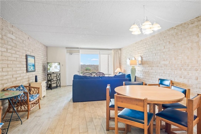 dining area featuring light wood-type flooring, a chandelier, and brick wall