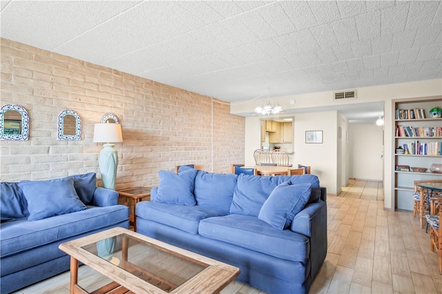 living room featuring an inviting chandelier, light wood-type flooring, and brick wall