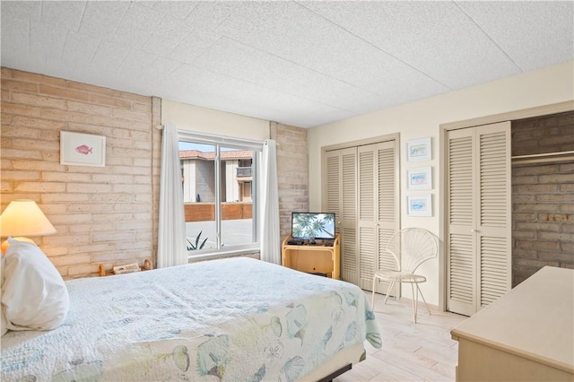 bedroom featuring brick wall, light hardwood / wood-style flooring, and two closets