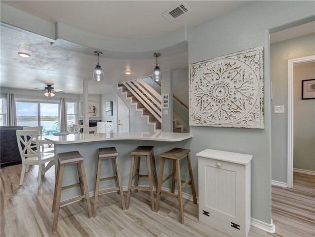 kitchen with light hardwood / wood-style floors, kitchen peninsula, ceiling fan, a breakfast bar area, and decorative light fixtures