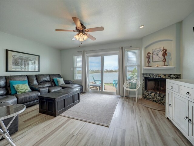 living room with a fireplace, a water view, ceiling fan, and light hardwood / wood-style flooring