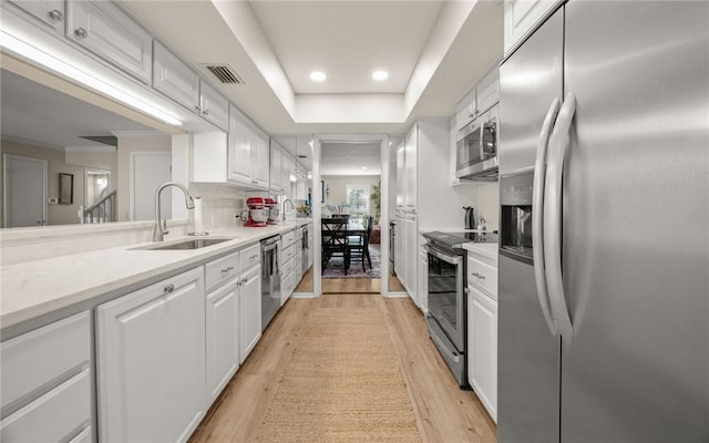 kitchen featuring sink, light stone counters, light wood-type flooring, stainless steel appliances, and white cabinets