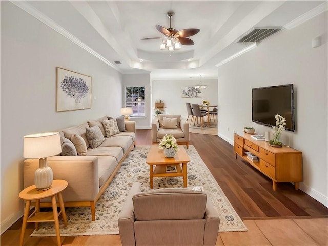 living room featuring ceiling fan, ornamental molding, wood-type flooring, and a raised ceiling