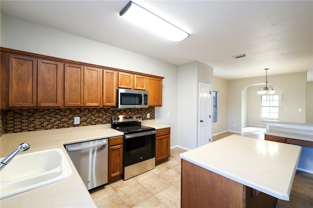 kitchen featuring decorative light fixtures, sink, backsplash, light tile patterned floors, and stainless steel appliances