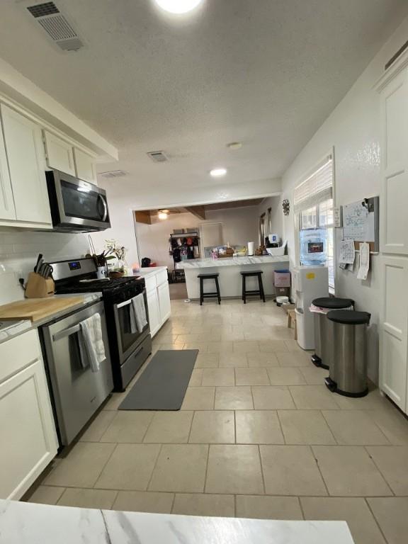 kitchen with appliances with stainless steel finishes, white cabinetry, light countertops, and light tile patterned floors