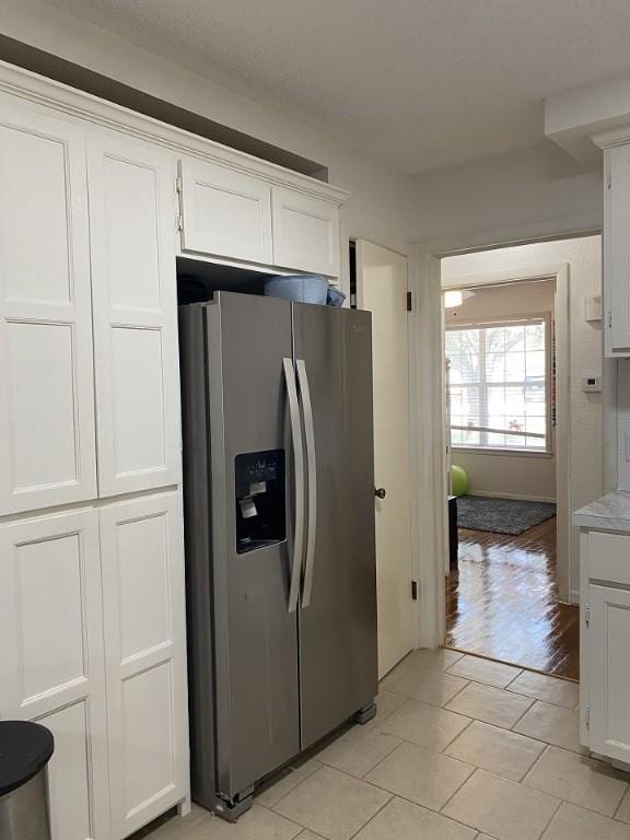 kitchen with stainless steel fridge, white cabinets, light countertops, and light tile patterned flooring