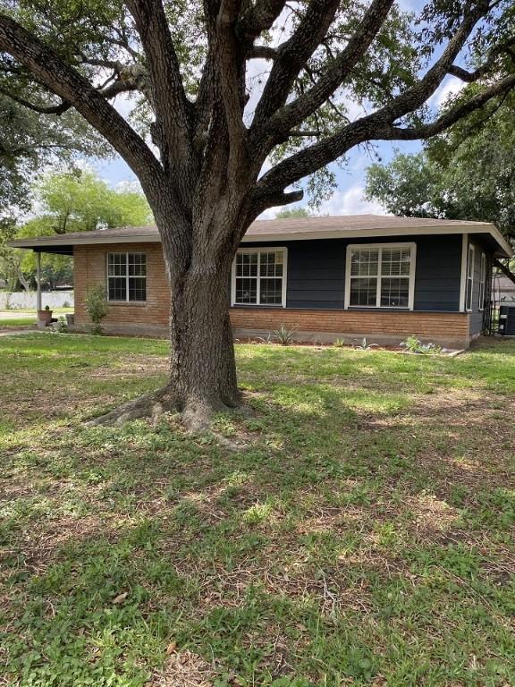 single story home featuring brick siding, a front yard, and central AC unit