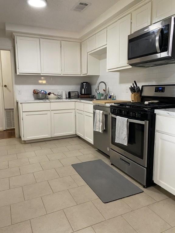 kitchen with stainless steel appliances, a sink, backsplash, and white cabinets